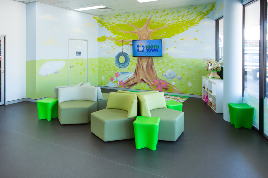 The Tooth Town waiting room: a painted tree mural, soft green seating and a play area